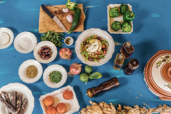 An overhead shot of a blue table laden with various fresh ingredients, plates, and cooking utensils, suggesting meal preparation.